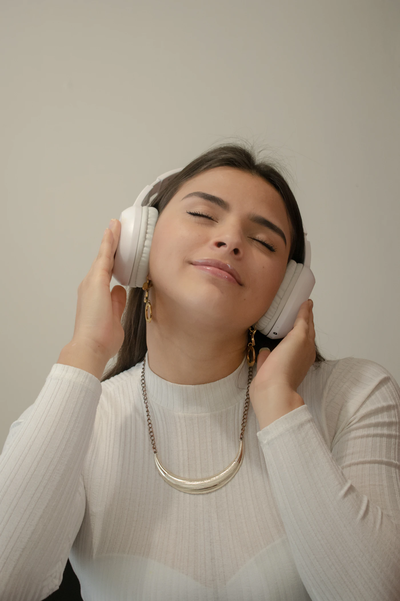 A woman in a white long-sleeved shirt wearing white headphones with eyes closed