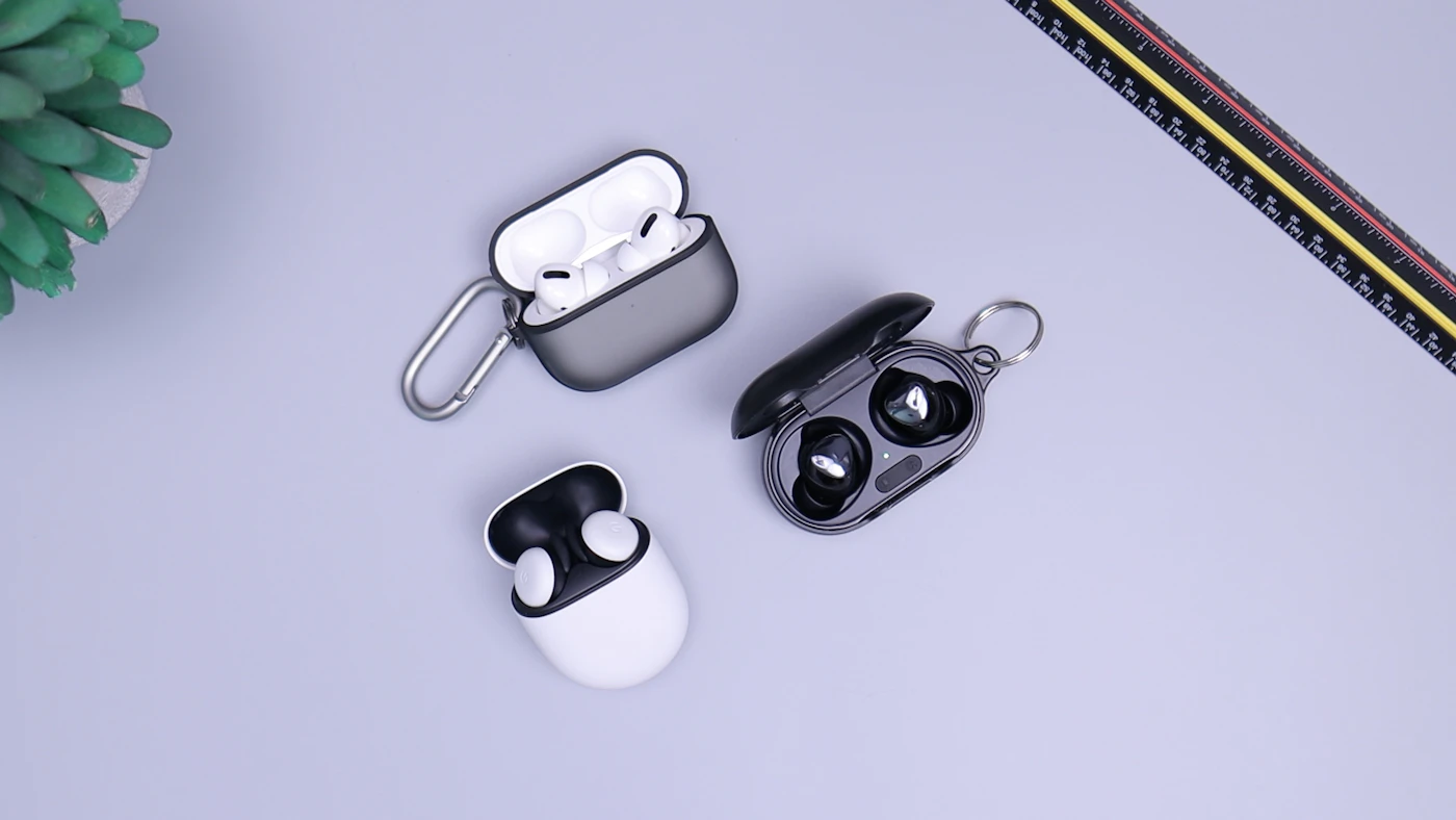 Three sets of wireless earbuds in charging cases on a tabletop